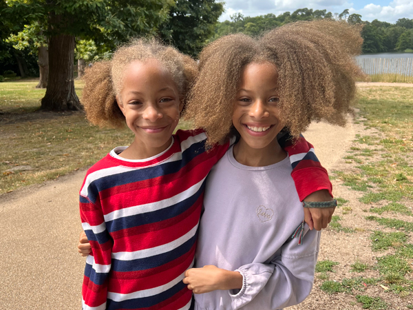 A pair of twins smile at the camera stood in a park