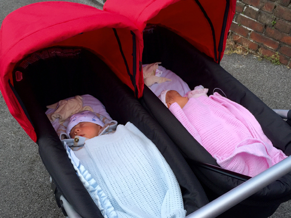 Two babies sleeping in a side-by-side double buggy