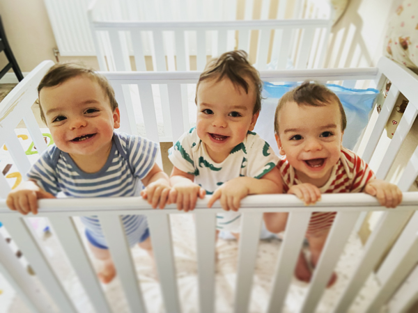 Three triplets stand looking out of a cot