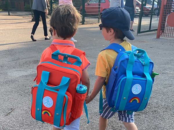 Two twin boys walk away from the camera with school bags on their backs