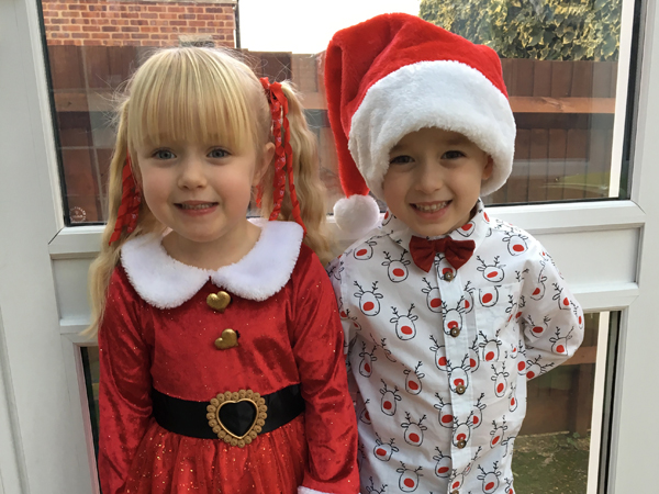 A young girl and boy wearing Christmas themed clothing pose for the camera