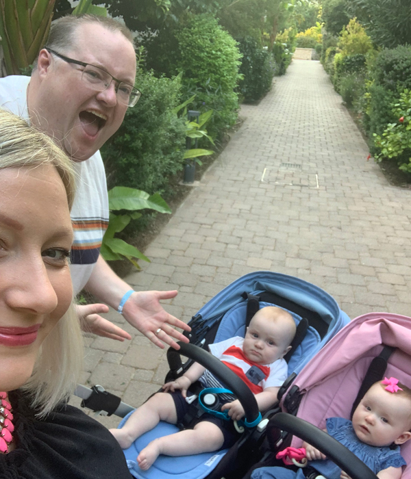 Two parents on the left take a selfie with their twin children in a buggy