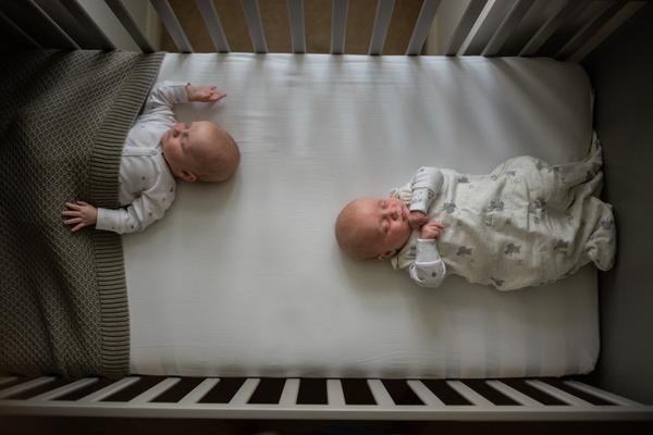 Overhead image looking down on twins sleeping in the feet-to-foot position at opposite ends of a cot