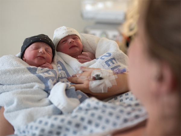 A picture taken looking over a woman's shoulder as she holds two new born babies