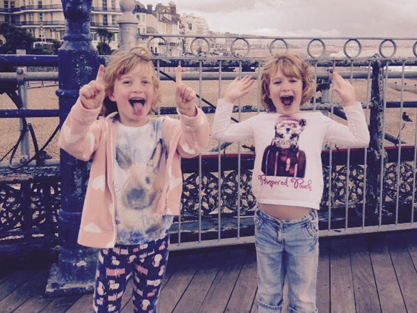Twin girls pull faces at the camera whilst standing by the seaside