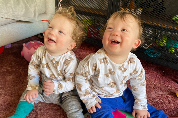 Two twins sit on the floor laughing