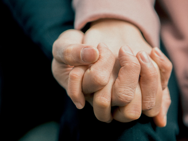 Close-up image of two people holding hands supportively