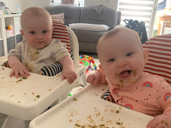 Twin babies sat in high chairs smiling at the camera
