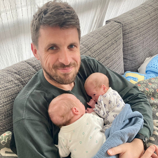 A father sits holding twin babies