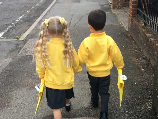 A boy and a girl in yellow school uniform walk together with their backs to the camera
