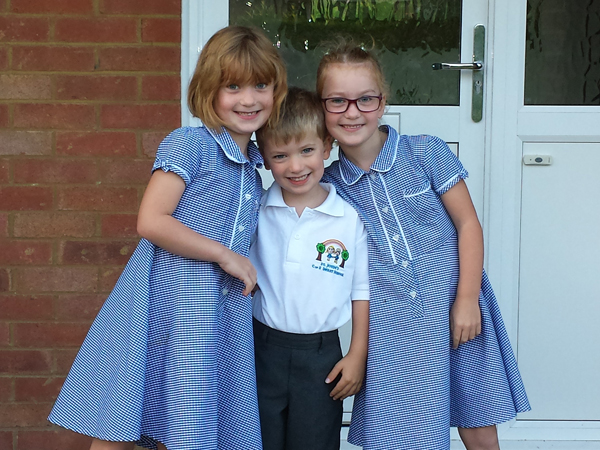 A younger brother stands behind two older sisters, all in primary school uniform